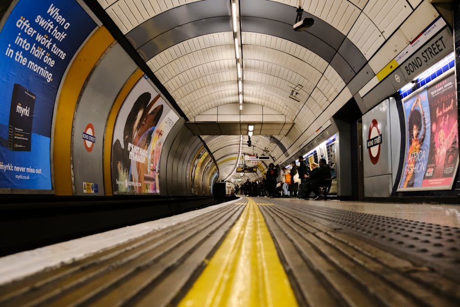 A close-up view of the London Underground sign, featuring a circular red border with a blue horizontal bar displaying the word 'UNDERGROUND' in white capital letters. The sign is mounted on a white po
